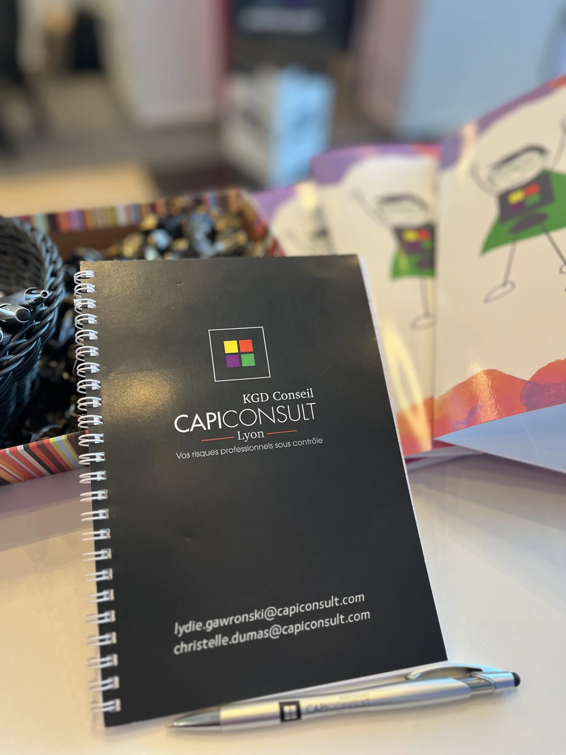 Carnet CAPICONSULT et stylo posés sur un bureau, avec des supports illustrés en arrière-plan
