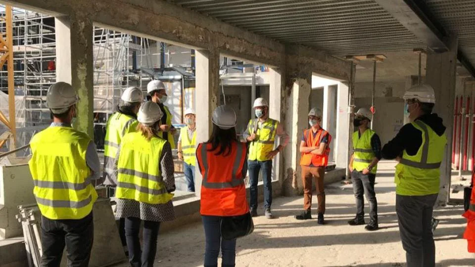 Groupe de personnes en casques et gilets haute visibilité dans un bâtiment en construction.